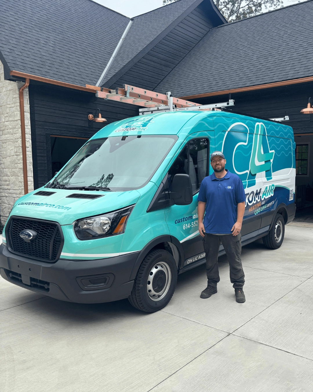 HVAC technician standing next to a Custom Air service van parked in a residential driveway, with a house and garage in the background.